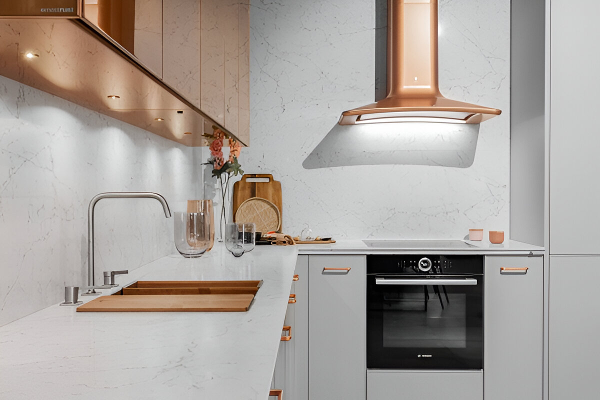 مطبخ حديث بتصميم أنيق يضم أجهزة وأسطح بلون نحاسي وجدران رخامية بيضاء